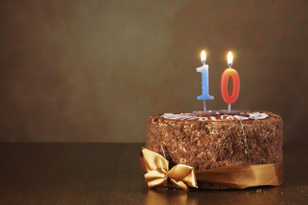Birthday chocolate cake with burning candle as a number ten on brown background