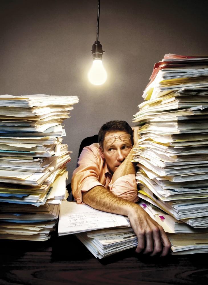 Overwroked businessman resting with stacks of documents on desk.