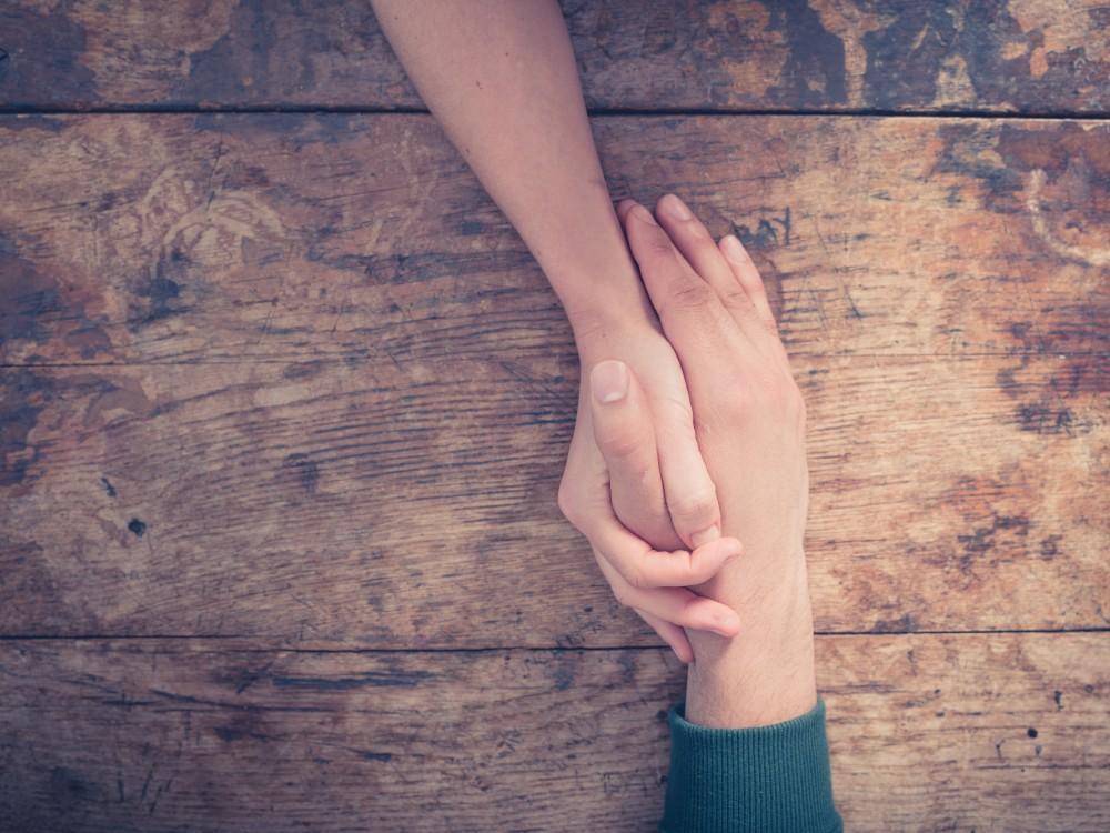 Close up on a man and a woman holding hands at a wooden table