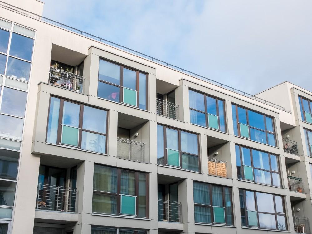 Low Angle Exterior View of Contemporary Low Rise Apartment Building with Small Balconies and Large Windows with Cloudy Blue Sky in Background