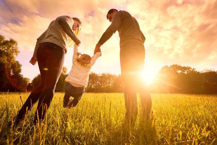 Happy family in the park evening light. The lights of a sun. Mom, dad and baby happy walk at sunset. The concept of a happy family.Parents hold the babys hands.