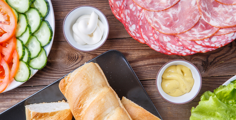 Components for baguette with sausage and vegetables on wooden table